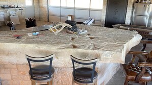 A spacious kitchen with a large island, bar stools, and a stone wall. - Bunkhouse in Texas ranch country (Guthrie)