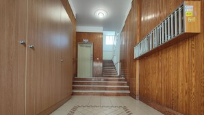 A hallway with wooden paneling, a tiled floor with a geometric pattern, and a staircase leading to an upper level.