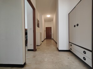 Een gang met een witte kast, een houten deur aan het einde, en een radiator aan de muur.