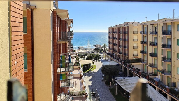 A view of a coastal residential area with multi-story buildings, a clear sky, and the sea in the background.