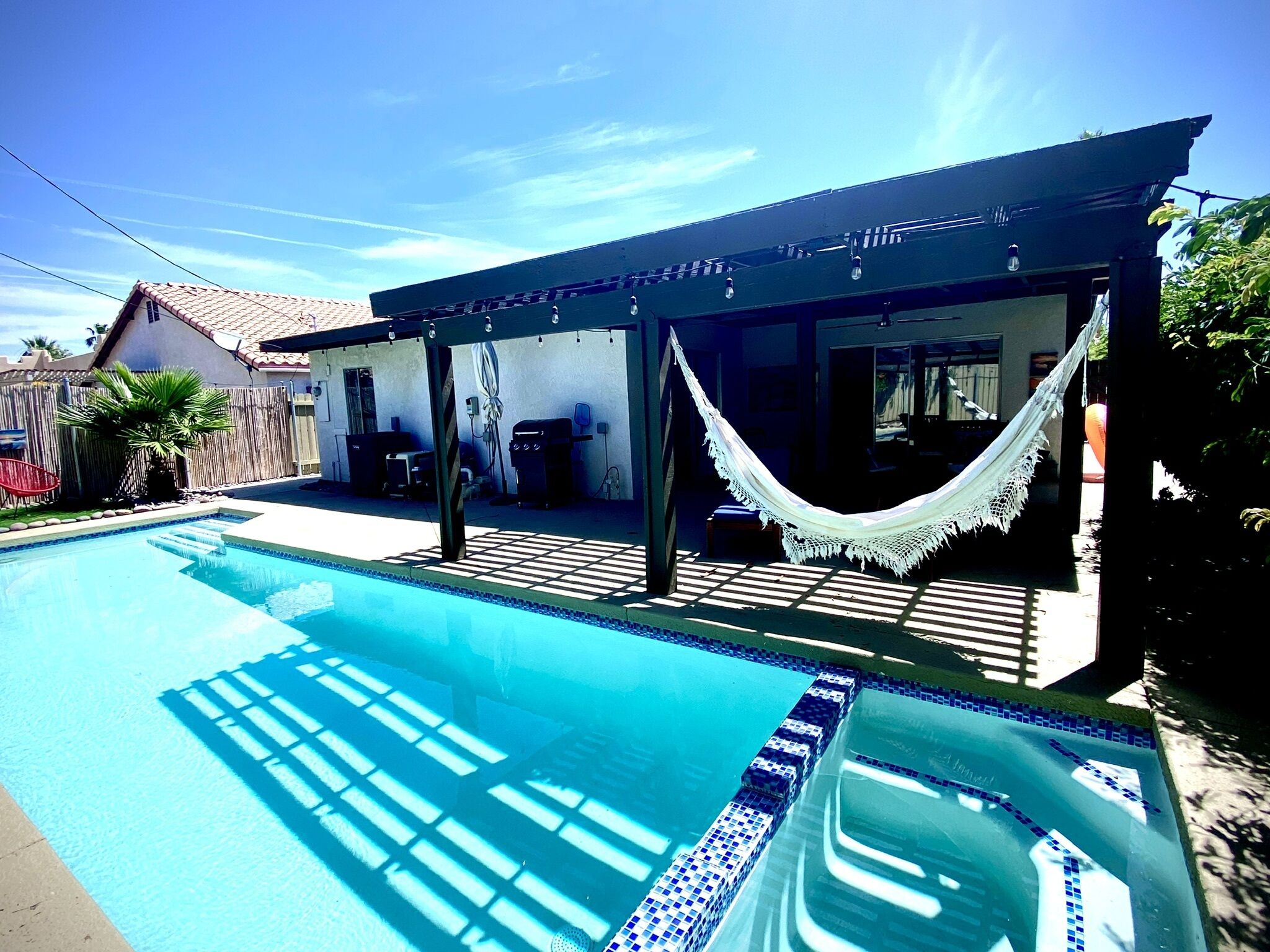 Una piscina con borde de azulejos, una hamaca y un área de patio techada.