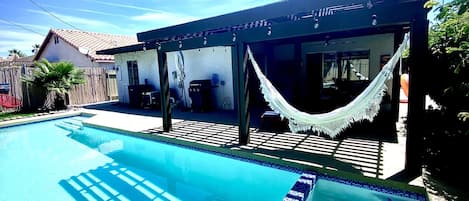Una piscina con borde de azulejos, una hamaca y un área de patio techada.