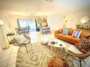 Ein Wohnzimmer mit einer Couch, Sesseln, einem Couchtisch und einem Essbereich, mit einer Küche im Hintergrund.