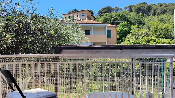 A balcony with a mesh fence, a chair, and a view of a building and trees. - Carminati 156 by Tempovacanza (Marina di Andora)