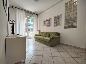 A living room with a green sofa, a white cabinet, and a large window with curtains.
