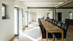 A long wooden dining table with black chairs, a vase of flowers, and a modern interior with large windows and a high ceiling. - Stylishly furnished fieldstone barn with dining room and terrace by the village pond (Werneuchen)