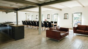 A spacious room with a long table and chairs, a leather sofa, and a kitchen area. - Stylishly furnished fieldstone barn with dining room and terrace by the village pond (Werneuchen)