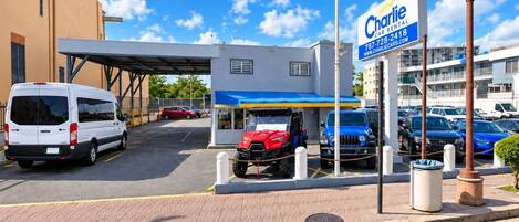A car rental station with a Charlie Rental sign, a covered parking area, and a building with multiple windows.