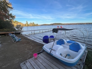 A boat docked at a wooden pier with a covered seating area and lounge chairs.