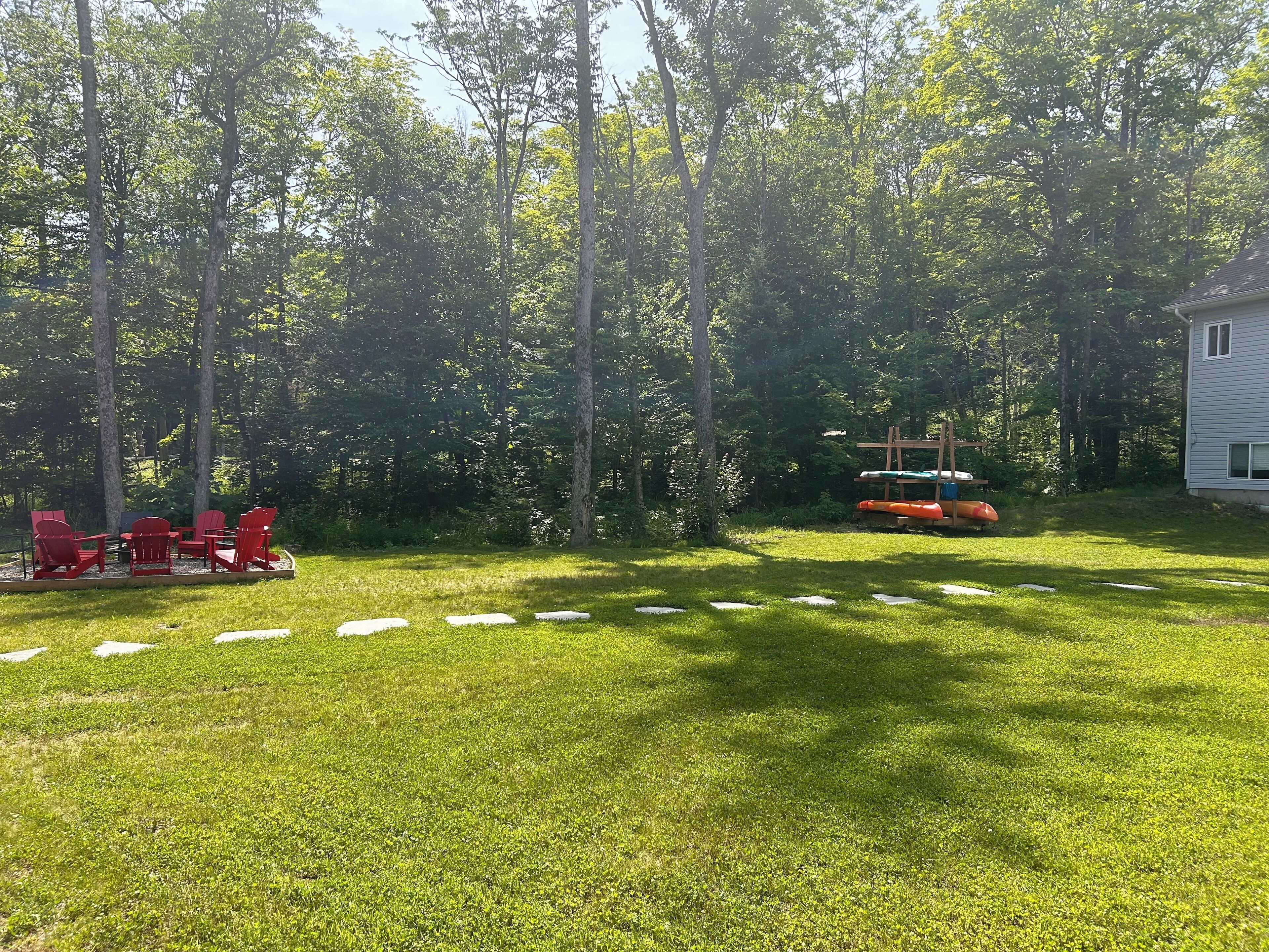 A backyard with a lawn, red Adirondack chairs, a wooden deck, and a play structure.