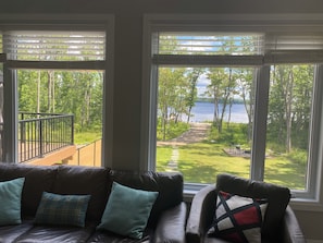 A room with a view of a lake, a balcony with a railing, and a sofa with cushions.