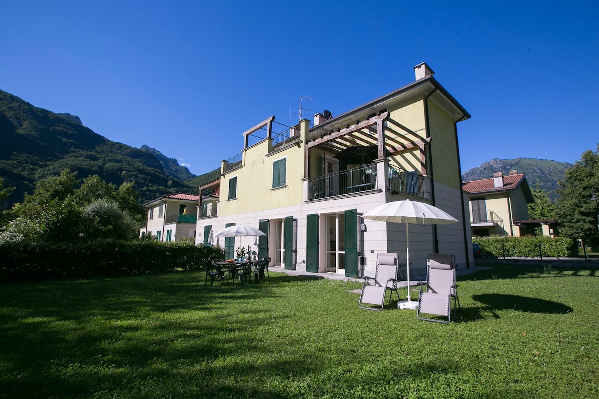 A two-story building with a balcony, outdoor seating, and a grassy yard.