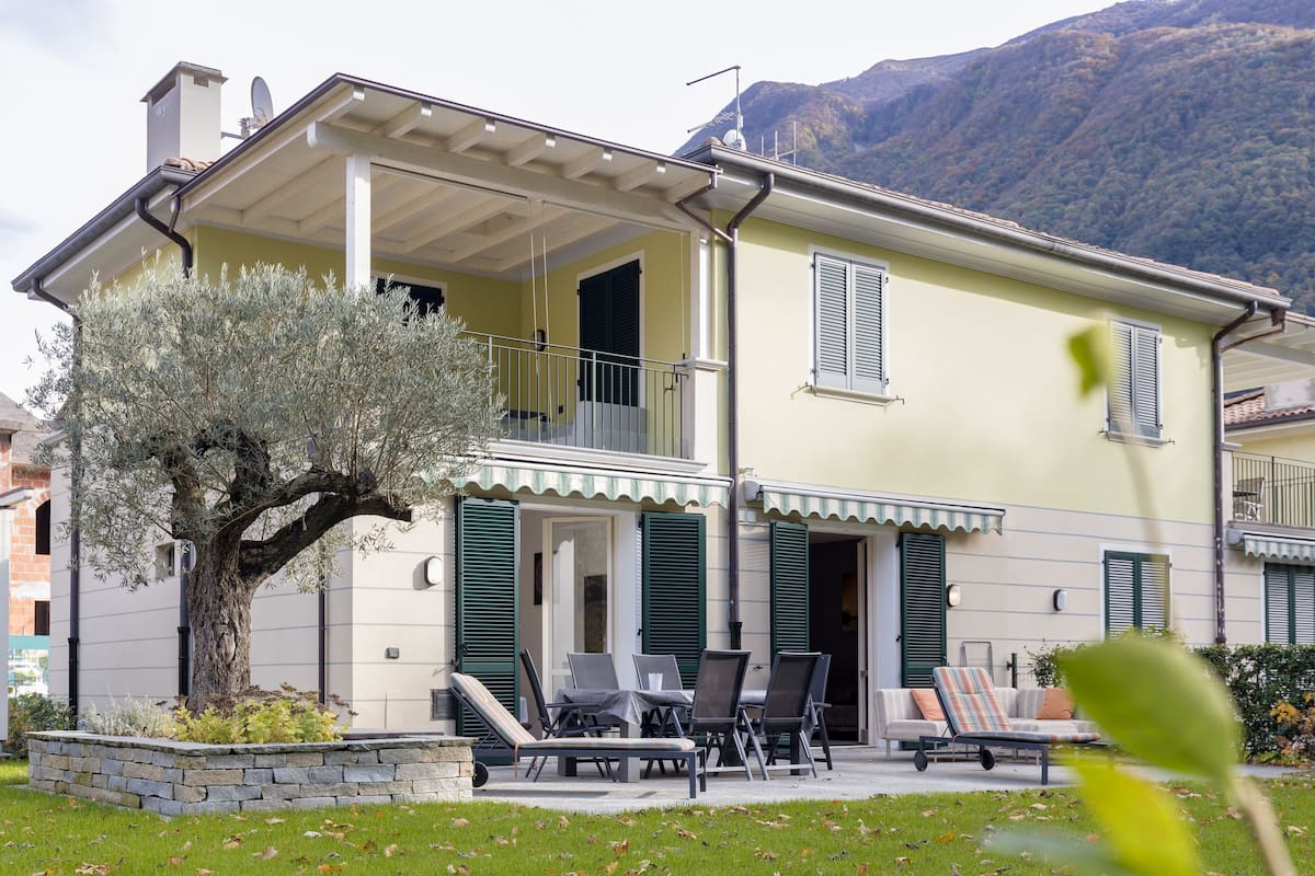 A two-story house with a balcony, outdoor seating, and a tree in the garden.