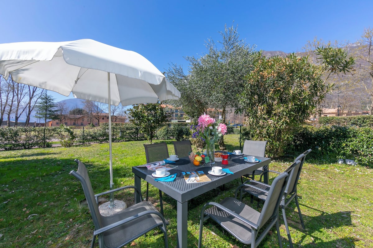 An outdoor table with chairs, a white umbrella, and a vase with flowers.