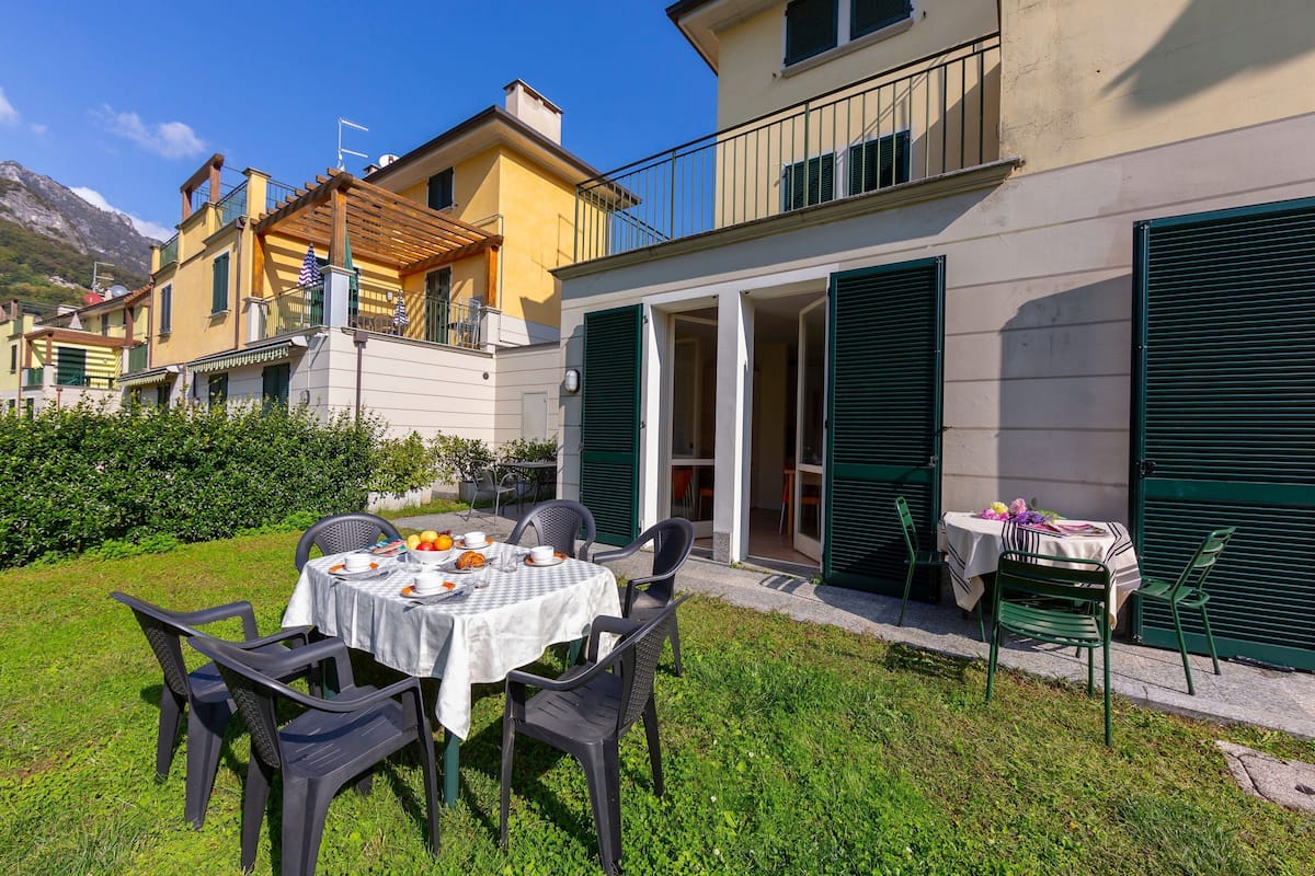 A patio with a table set for two, surrounded by chairs, and a small table with a tablecloth and items on it.