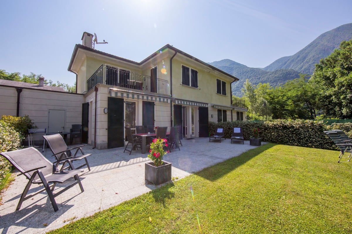 A two-story house with a balcony, outdoor seating, and a garden.