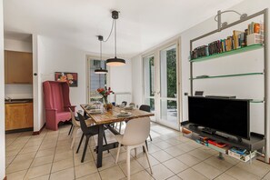A dining area with a wooden table, chairs, a television, and a bookshelf. - Villa Apartments - Porto Letizia (Porlezza)
