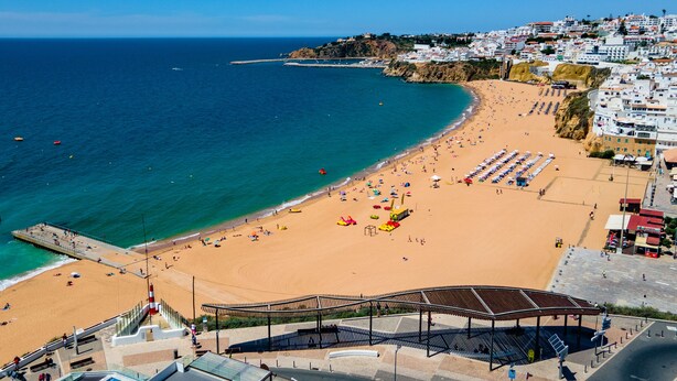 Una playa costera con un paseo marítimo, sombrillas de playa y una amplia zona abierta con asientos.