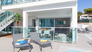 Un espacio exterior moderno con dos sillones de descanso, una mesa de comedor con sillas, una escalera y una piscina.