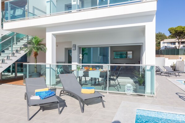 A modern outdoor area with two lounge chairs, a dining table with chairs, a staircase, and a pool.