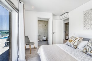 A modern bedroom with a large bed, a chair, and a view of the pool.