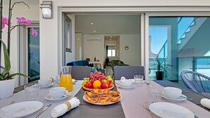 Una mesa de desayuno dispuesta con platos, cubiertos, vasos y una cesta de fruta.