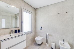A modern bathroom with a large mirror, a sink, a toilet, and a bidet.