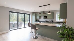 A modern kitchen with a large island, bar stools, and pendant lighting. - Fron Haul - Gwennol (Ruthin)