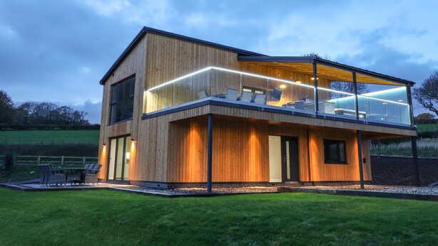 A modern two-story wooden house with a glass balcony and outdoor seating area. - Fron Haul - Gwennol (Ruthin)