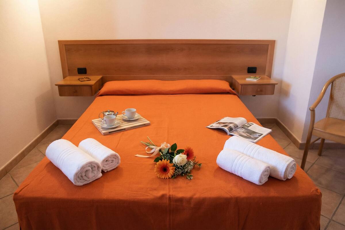 Quarto de hotel com uma cama grande, duas mesas de cabeceira, um painel de cama de madeira e uma cadeira.