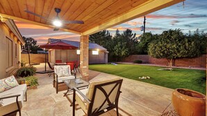 An outdoor patio with a table and chairs, a ceiling fan, and a view of the backyard. - Amenities Galore! Outdoor Living & Lots of Games (Peoria)