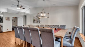 A dining area with a wooden table, grey upholstered chairs, a chandelier, and a ceiling fan. - Amenities Galore! Outdoor Living & Lots of Games (Peoria)