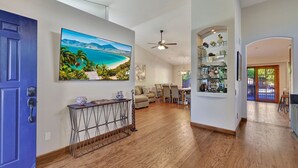 A spacious living area with a wooden floor, a blue door, and a painting of a beach scene. - Amenities Galore! Outdoor Living & Lots of Games (Peoria)