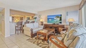 A living room with a sofa, armchairs, a coffee table, a TV, and a kitchen area in the background. - Beautiful Gulf views from this 9th floor condo - CL0902 (Naples)