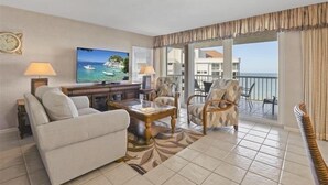 A living room with a sofa, armchairs, a coffee table, and a TV. There is a balcony with a view of the sea. - Beautiful Gulf views from this 9th floor condo - CL0902 (Naples)