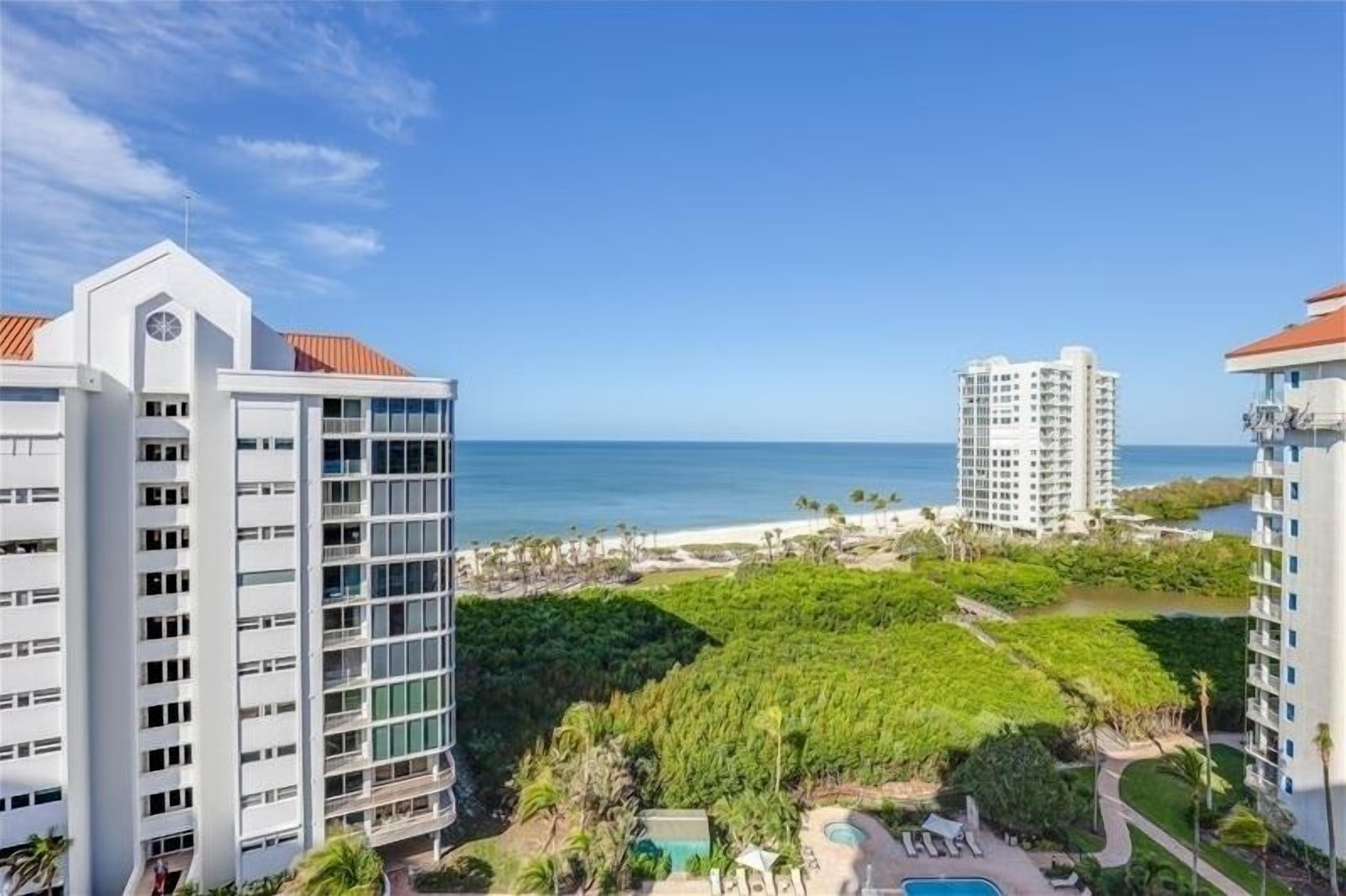 A high-rise hotel with a pool area, surrounded by lush greenery and a view of the ocean.