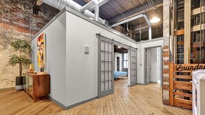 Una habitación amplia con una máquina grande de estilo industrial, suelo de madera, pared de ladrillo y un letrero que dice "Laundry".