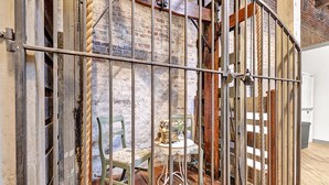 Una habitación rústica con paredes de ladrillo visto, una escalera de madera y una reja de metal.
