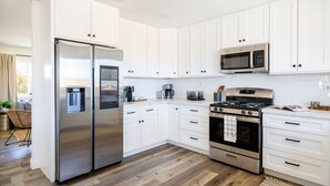 A modern kitchen with white cabinets, stainless steel appliances, and a wooden floor. - Boho🎨 Haus✦NearPark✦Views✦HotTub✦🎮Den✦🔥Pit✦Ev🔋 (Joshua Tree)