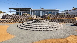 A modern house with a stone retaining wall and a circular driveway. - Boho🎨 Haus✦NearPark✦Views✦HotTub✦🎮Den✦🔥Pit✦Ev🔋 (Joshua Tree)