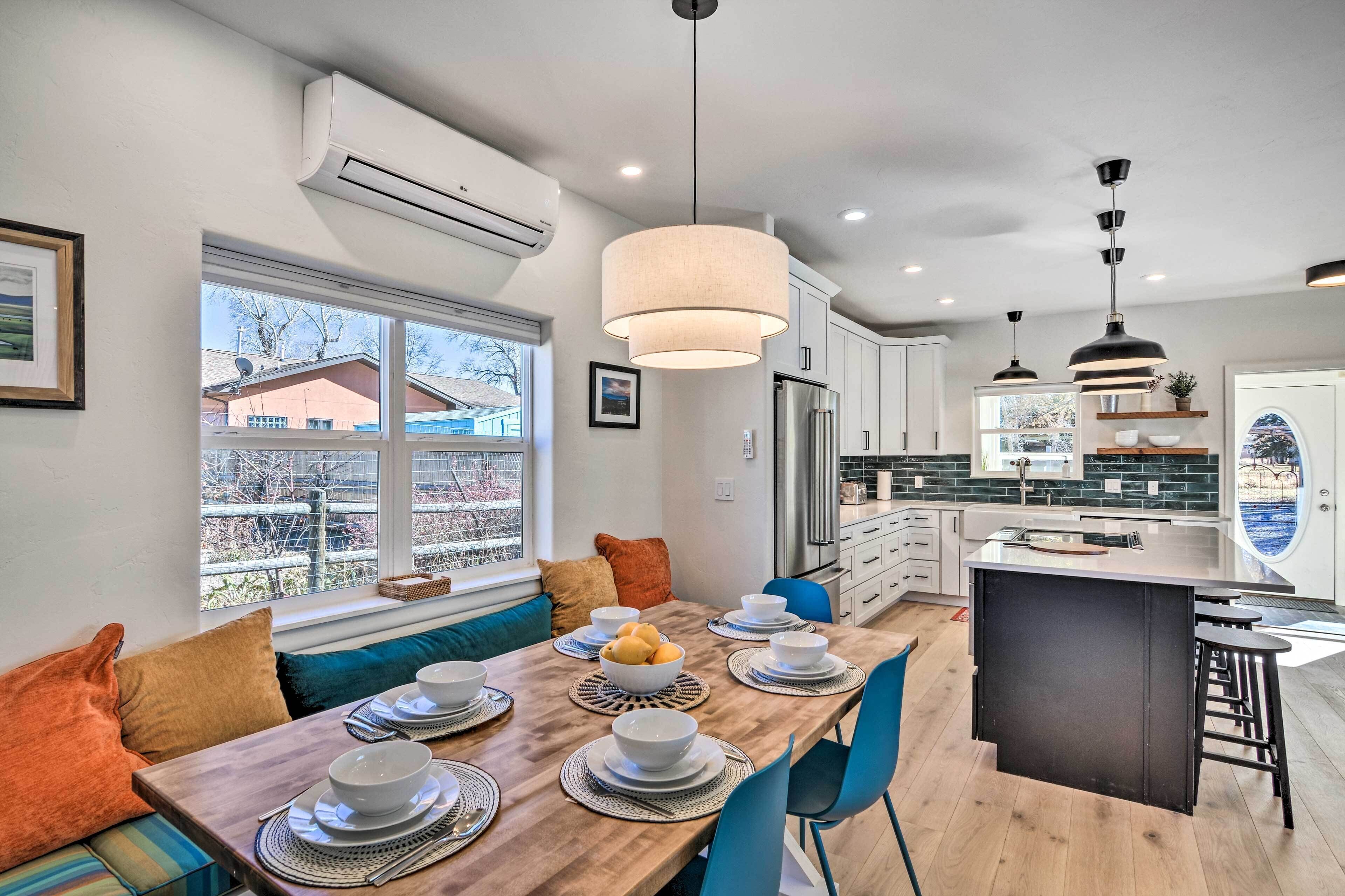 Een moderne keuken met een centraal eiland, een eethoek met een lange tafel voor vier personen, en een uitzicht op het buiten via grote ramen.