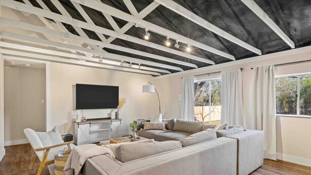 A modern living room with a sectional sofa, a flat-screen TV, and a ceiling with exposed beams. - Serene Getaway Near Baylor and Magnolia Perfect for Relaxation and Exploration (Waco)