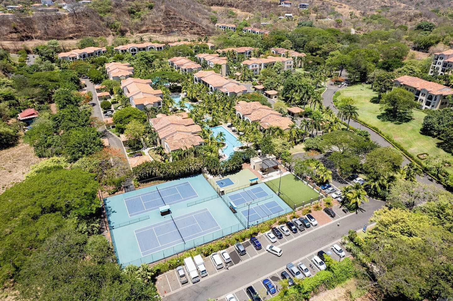 Vue aérienne d’un complexe hôtelier comprenant plusieurs villas, un court de tennis et une piscine.