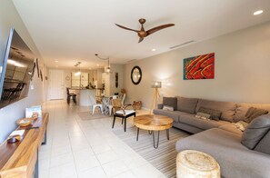 A modern living room with a sofa, a dining area with chairs, a wooden table, and a ceiling fan.