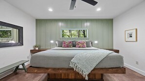Un dormitorio con cama, ventana, espejo y un cuadro en la pared.