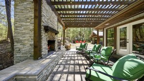 A stone fireplace with a fire, outdoor seating, and a pergola with string lights.