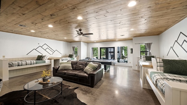A spacious living area with a pool table, leather sofa, and a glass coffee table.