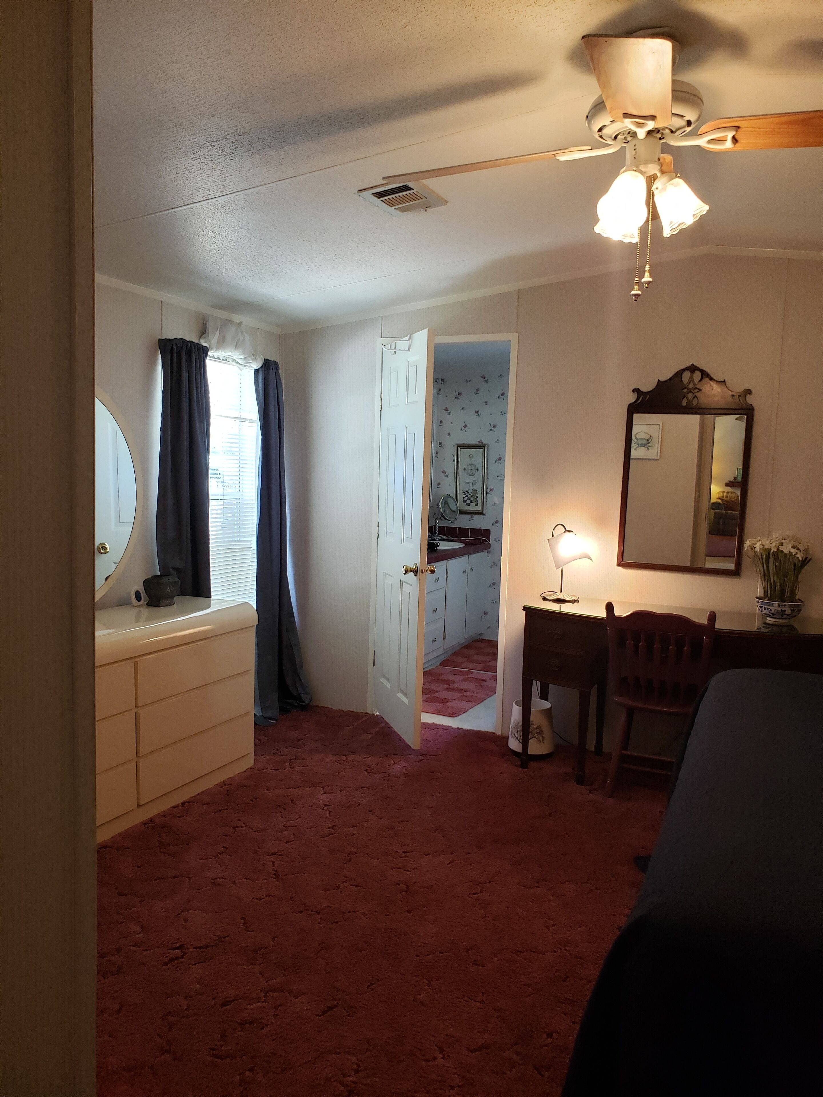 A bedroom with a bed, a dresser, a chair, a desk, a mirror, and a ceiling fan.