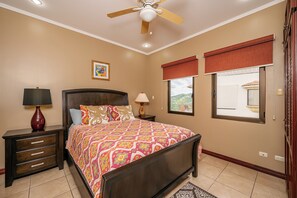 Une chambre à coucher comprenant un lit, des tables de chevet, un ventilateur de plafond, une fenêtre avec vue et un luminaire fixé au mur.