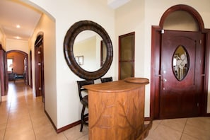 A hallway with a wooden reception desk, a large mirror, and a wooden door with a glass panel. - RECENTLY UPDATED • Villa Lorenzo • 3 BR Oceanview Penthouse Villa • 6 Guests (Playa Hermosa)